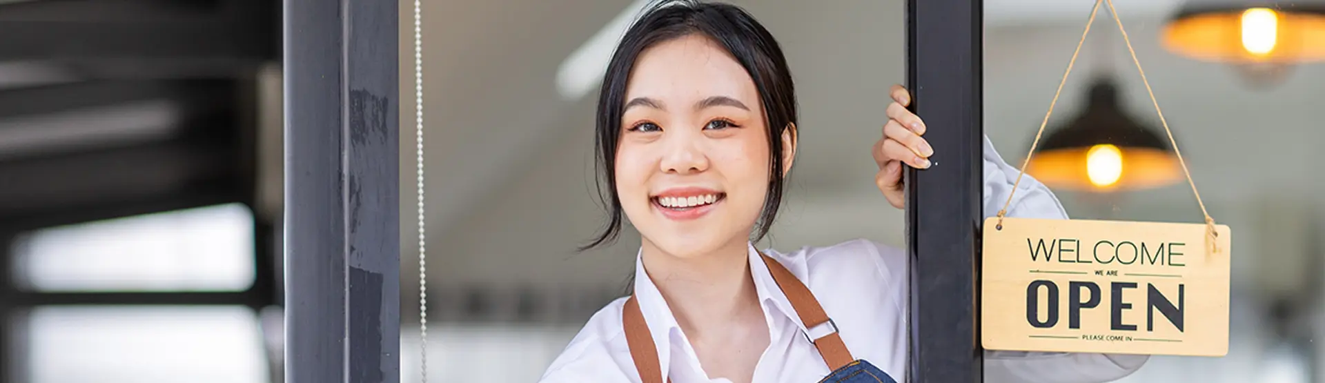 An young Asian girl leaning by the store door with a Welcome Open sign  