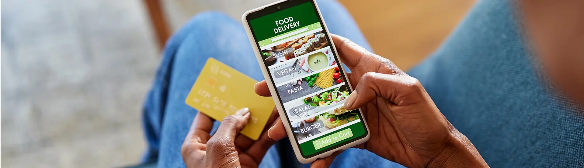 A cardholder placing an online order on a mobile phone while holding a credit card.